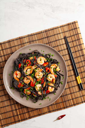 Black pasta with roasted prawns. Served on a plate. Stone background. Chopsticks or fork.の写真素材