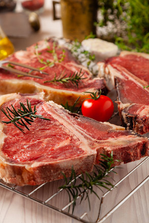 Raw t bone steak, with herbs. Grill accessories. Ready for grilling. Wooden bright background.の写真素材