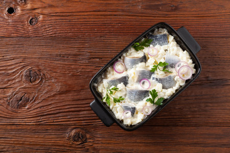 Herring fillet salad in cream with apple. Served in a black briquette. Wooden background.の写真素材
