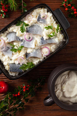 Herring fillet salad in cream with apple. Served in a black briquette. Wooden background. Christmas decoration.の写真素材