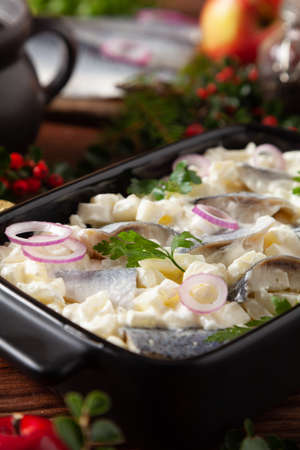 Herring fillet salad in cream with apple. Served in a black briquette. Wooden background. Christmas decoration.の写真素材