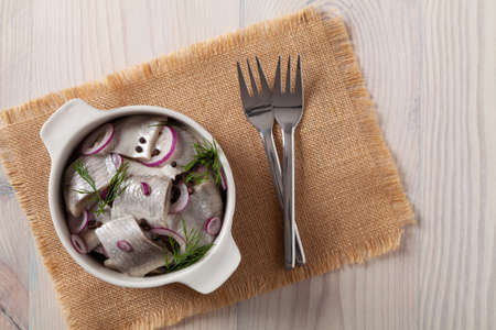 Herring fillets in oil. Served with onion in a bowl. Wooden background.の写真素材