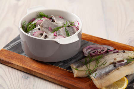Herring fillets in oil. Served with onion in a bowl. Wooden background.の写真素材