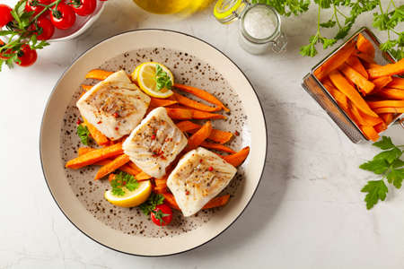 Fried pieces of cod loin, served with sweet potato fries. Light stone background.の写真素材