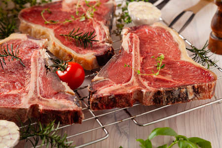 Raw t bone steak, with herbs. Grill accessories. Ready for grilling. Wooden bright background.の写真素材