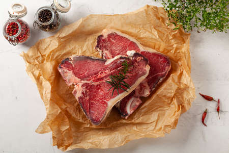 Raw t bone steak, served on paper. Herbs, stone background.の写真素材