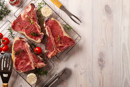 Raw t bone steak, with herbs. Grill accessories. Ready for grilling. Wooden bright background.の写真素材