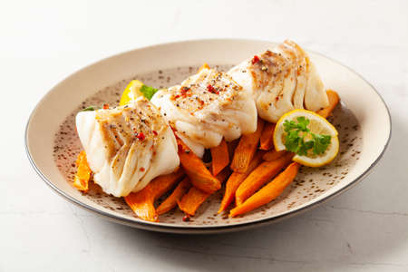 Fried pieces of cod loin, served with sweet potato fries. Light stone background.の写真素材