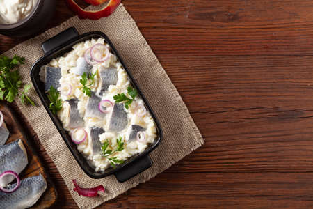 Herring fillet salad in cream with apple. Served in a black briquette. Wooden background.の写真素材