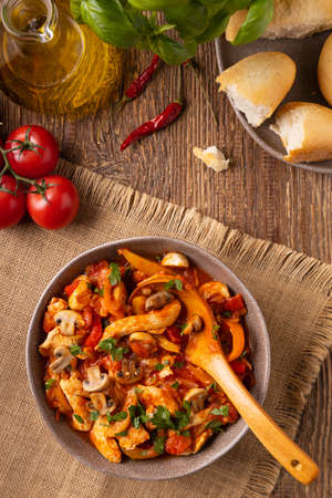 Chicken stew with peppers, mushrooms and tomatoes. Wooden background.の写真素材