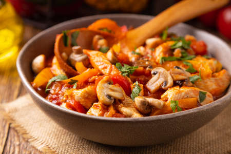 Chicken stew with peppers, mushrooms and tomatoes. Wooden background.の写真素材