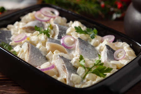 Herring fillet salad in cream with apple. Served in a black briquette. Wooden background. Christmas decoration.の写真素材