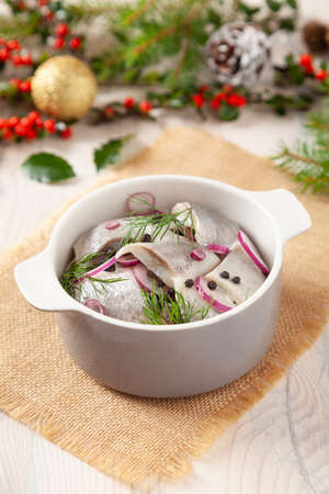 Herring fillets in oil. Served with onion in a bowl. Wooden background. Christmas decorationの写真素材