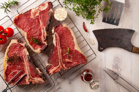 Raw t bone steak, with herbs. Grill accessories. Ready for grilling. Wooden bright background.の写真素材