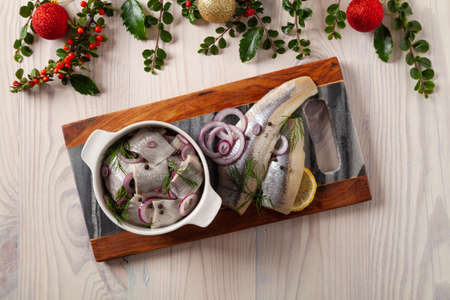 Herring fillets in oil. Served with onion in a bowl. Wooden background. Christmas decorationの写真素材