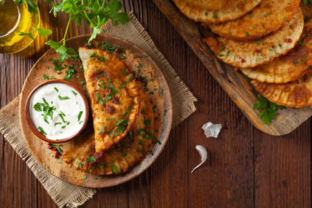 Traditional cheebureki, served on a wooden plate with sauce. Decorated with parsley.の写真素材