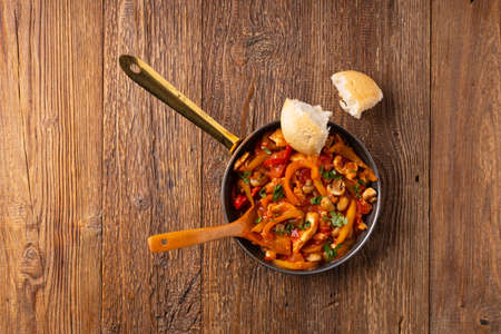 Chicken stew with peppers, mushrooms and tomatoes. Wooden background.の写真素材