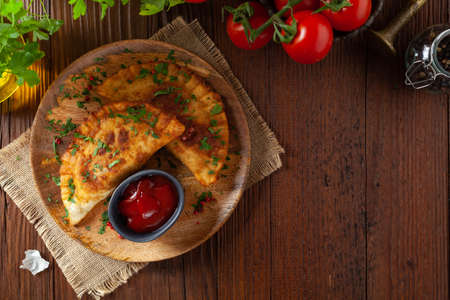 Traditional cheebureki, served on a wooden plate with sauce. Decorated with parsley.