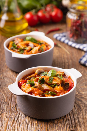 Chicken stew with peppers, mushrooms and tomatoes. Wooden background.の写真素材