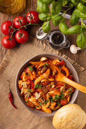Chicken stew with peppers, mushrooms and tomatoes. Wooden background.の写真素材