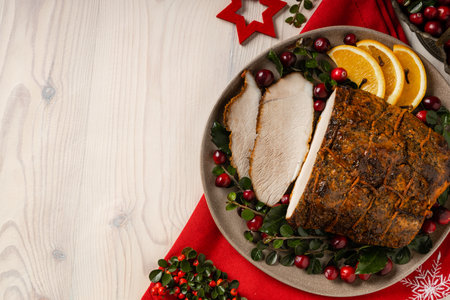 Whole baked ham. Christmas decoration. Served with cranberries and oranges. Tied with string during baking. Wooden table.の写真素材