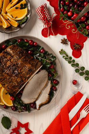 Whole baked ham. Christmas decoration. Served with cranberries and oranges. Tied with string during baking. Wooden table.の写真素材