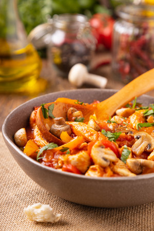 Chicken stew with peppers, mushrooms and tomatoes. Wooden background.の写真素材