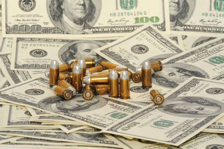 Handgun Cartridges on Background with Many American Handred Dollar Bills.