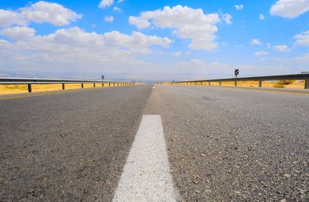 Empty Highway in Desert Near Dead Sea, Israel, Against Blue Sky with Clouds.