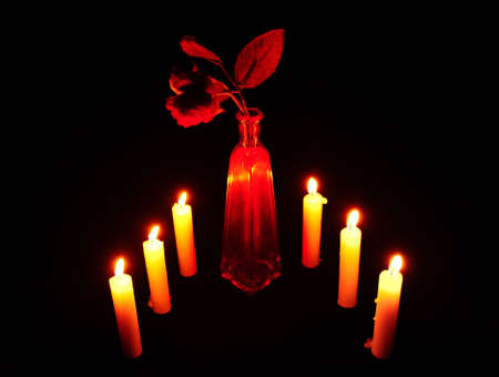 Rose in a Red Vase, Surrounded by Burning Candles on a Black Backgroundの写真素材
