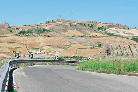 Winding Asphalt Road on the Background of the Modern Wind Turbines in Sicilyの写真素材