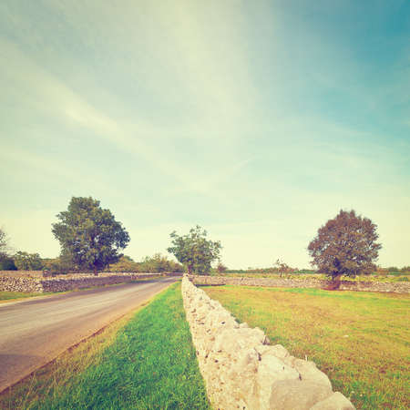 Asphalt Road along the Pasture Divided into Section by the Stone Wall, Vintage Style Toned Pictureの写真素材