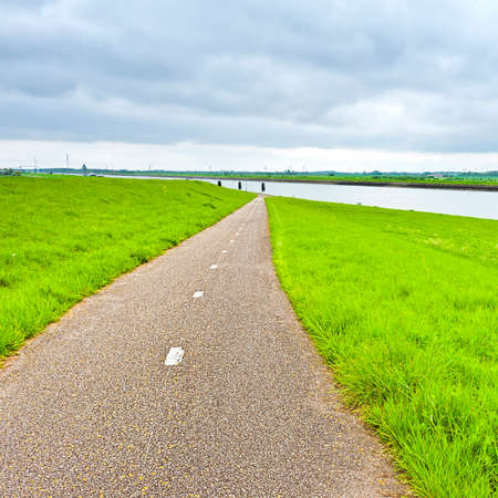 Agriculture on Land Reclaimed from the See in Netherlands. Asphalt road along protective dam and canal in Hollandの写真素材