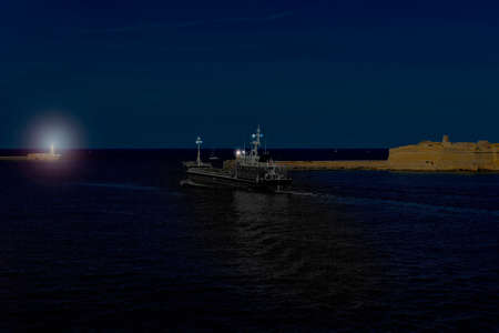 Cargo ship leaves the harbor of Valletta at night. Lighthouses indicate the entrance to the ports of Maltaの写真素材