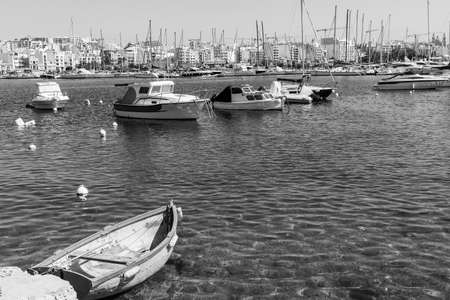Yachts docked at the port of Malta. Boats moored in a row on the background of modern city. A shabby old boat among the luxury ships. Black and white pictureの写真素材