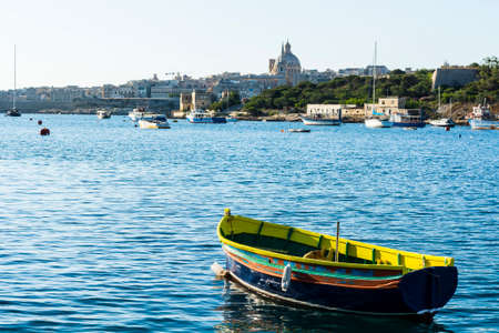 Cityscape view with Basilica of Our Lady of Mount Carmel on the island of Malta. Yachts docked at the port of Valletta. A shabby old boat among the luxury shipsの写真素材