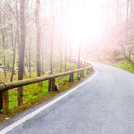 Morning mist over the asphalt road in the Italian Alps in Piedmont. View of the mountain valley with highway at sunriseの写真素材