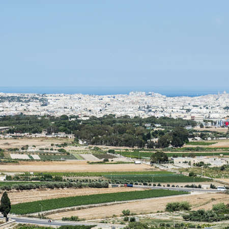 Rural landscape with asphalt roads and fields on Malta. Maltese city on the background of Mediterranean sea.の写真素材