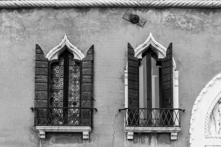 Ogival mosaic Venetian windows with shutter. Houses peeling off from dampness in Venice. Black and white pictureの写真素材