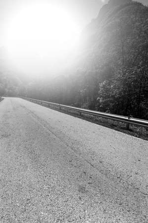 Morning mist over the asphalt road in the Italian Alps. View of the mountain valley with highway at sunrise. Black and white pictureの写真素材