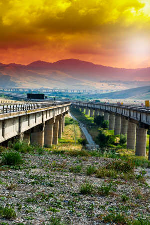 Landscape of Sicilian hills at sunrise. Asphalt road elevated by columns due of frequent earthquakes...