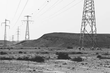 Desolate infinity of the Rocky hills of the Negev Desert in Israel. Electrical power lines on pylons in the landscape of the Middle East. Black and white photoの写真素材