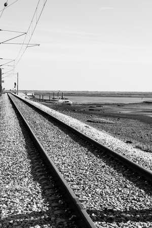 Railroad on the shore of Atlantic Ocean in Portugal. Electrified railway near nature park of Ria Formasa in Faro city. Black and white photoの写真素材