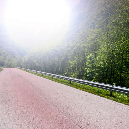 Morning mist over the asphalt road in the Italian Alps. View of the mountain valley with highway at...