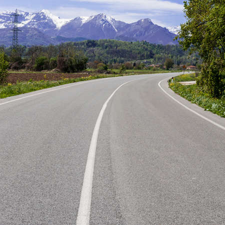 Asphalt road on the Background of Snow-capped Alps. High-voltage Power Line along the highway.