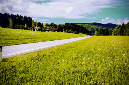 Asphalt road in Austrian landscape with forests, fields, pastures and meadows. Vintage styleの写真素材