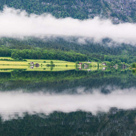 Rain and clouds on the Hallstattersee in Austria. Morning mist over the Austrian landscape with lake, forests, fields, pastures, meadows and villageの写真素材