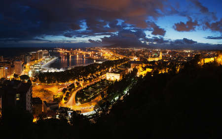 View of the Malaga city, Spain. Aerial view of City Hall and port with illuminated buildings at night with sunset skyの写真素材