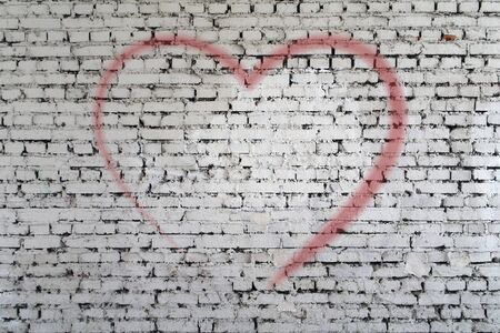 White brick wall painted with a red heart outlines the background texture.の写真素材