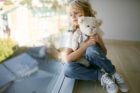 Teen beautiful girl in jeans clothes near the window with bearの写真素材